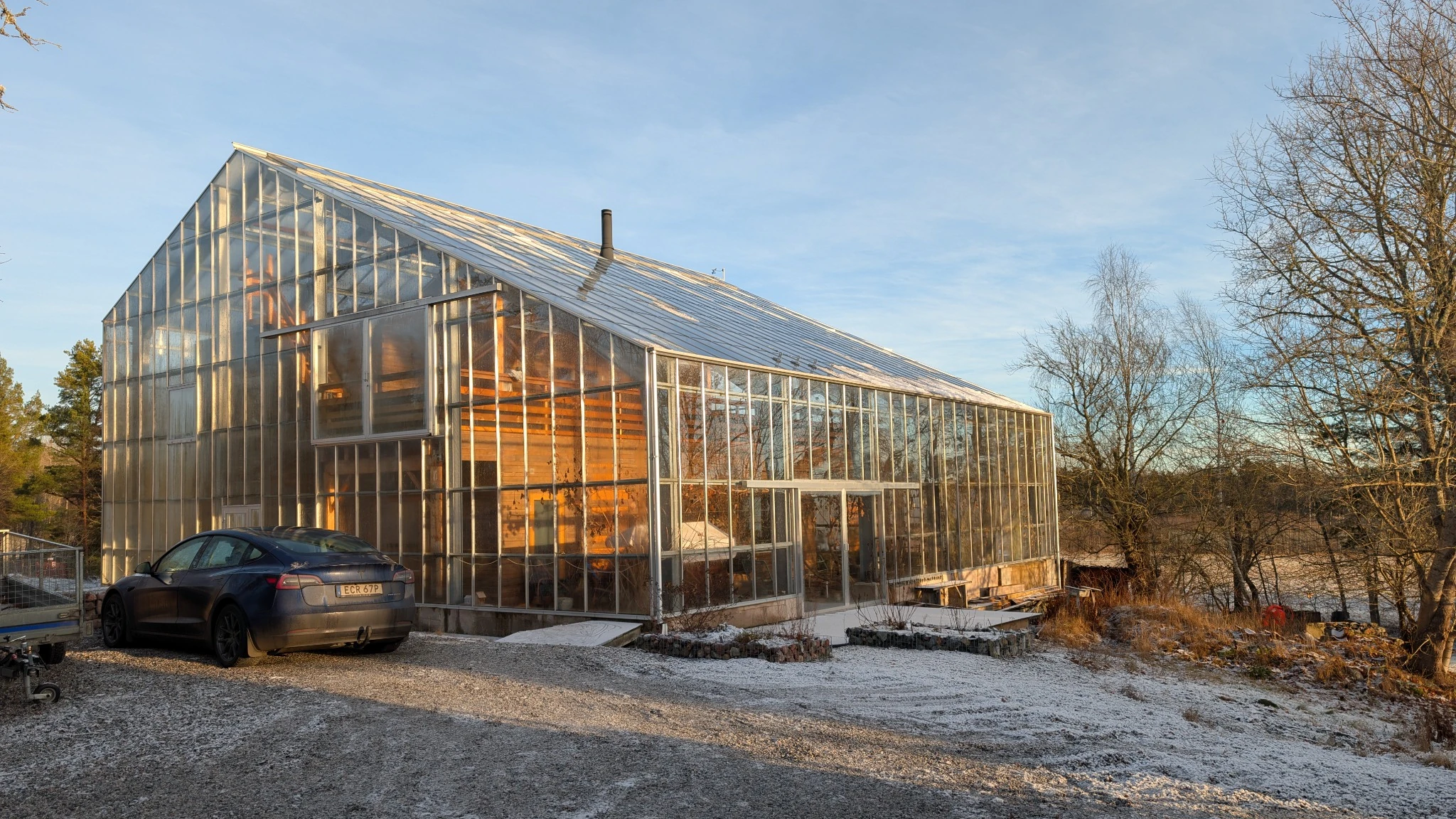Sundby Naturhus in low winter sunlight, showing the timber home inside its glass enclosure and frost on the ground.